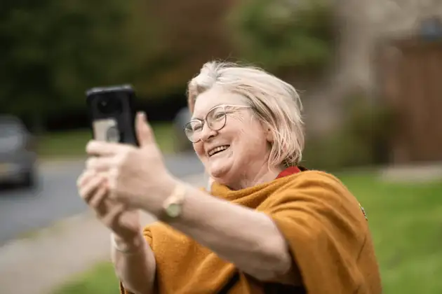 Woman smiling while taking a selfie on her phone outdoors